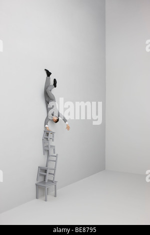 Imprenditore facendo handstand sulla sommità del precariamente sedie impilate Foto Stock