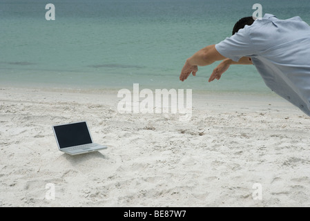 Uomo in spiaggia, piegarsi come se le immersioni nel computer portatile, vista ritagliata Foto Stock