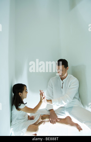 Padre e figlia seduta sul pavimento, toccando le mani Foto Stock