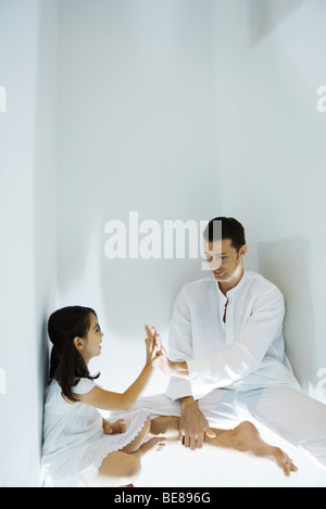 Padre e figlia seduta sul pavimento, toccando le mani Foto Stock