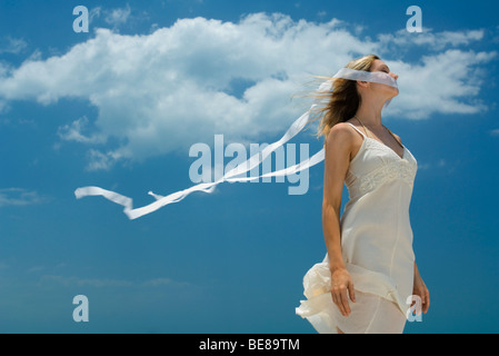 Donna con nastro che copre la bocca, estremità del nastro al vento contro il cielo blu Foto Stock