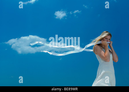 Donna che mantiene il nastro che copre la bocca, estremità del nastro al vento Foto Stock