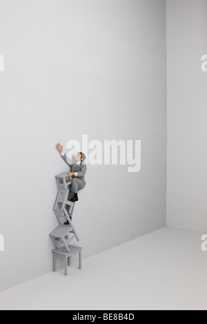 Imprenditore arrampicata e raggiungere la cima della scala fatta di sedie impilate Foto Stock