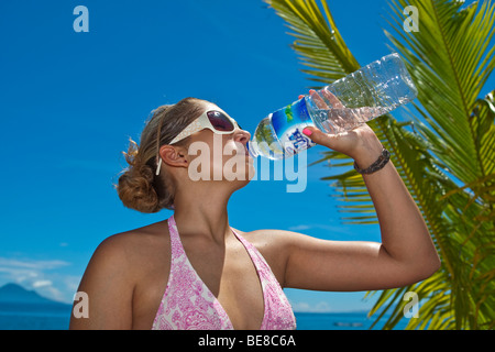 Giovane donna sulla spiaggia a bere da una bottiglia di acqua, Indonesia, sud-est asiatico Foto Stock