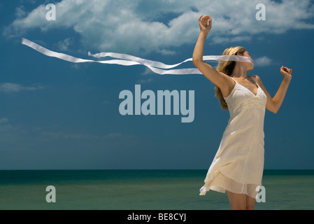 Donna in piedi con le braccia alzate, vento che soffia nastro attraverso la sua bocca di mare in background Foto Stock