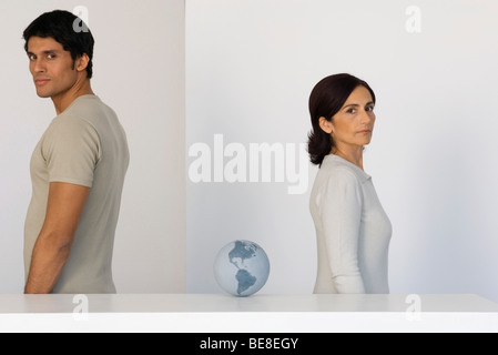 L uomo e la donna in piedi con le spalle rivolte al mondo seduto su un bancone tra di loro Foto Stock