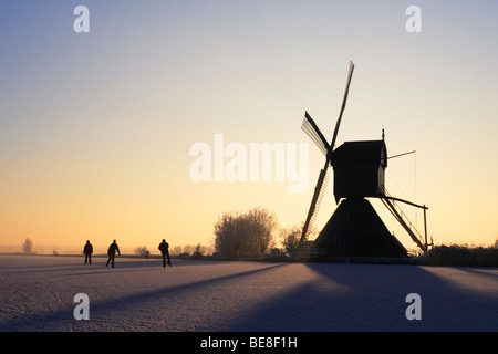 Pattinaggio sul ghiaccio pattino lungo i mulini a vento di Kinderdijk presso sunrise Foto Stock