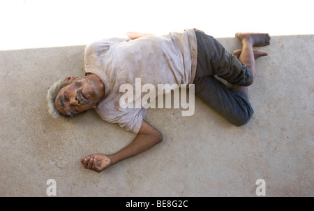 Un uomo senza tetto privi di casa, cibo, abbigliamento corretto e malati giace sul marciapiede. Foto Stock