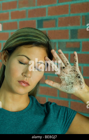 Donna con gli occhi chiusi tenendo la mano alla testa che mostra sporco palm Foto Stock