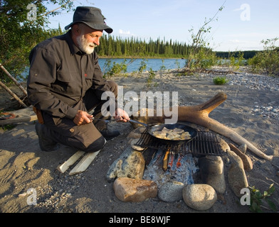 Uomo di cottura, friggere i filetti di pesce in una padella su un fuoco di campo superiore del Fiume Liard, Yukon Territory, Canada Foto Stock