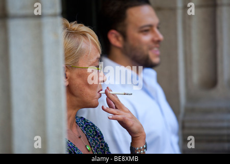 Donna di fumare al di fuori di un edificio per uffici nel Quartiere Finanziario di New York City Foto Stock