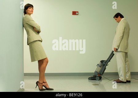 Ben vestito donna appoggiata contro la parete con le braccia incrociate, uomo di aspirare in background Foto Stock