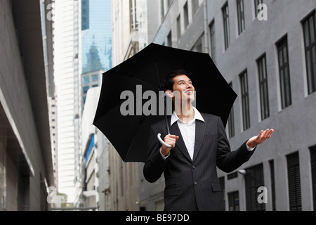 Asian businessman holding ombrello, guardando in alto nel cielo Foto Stock
