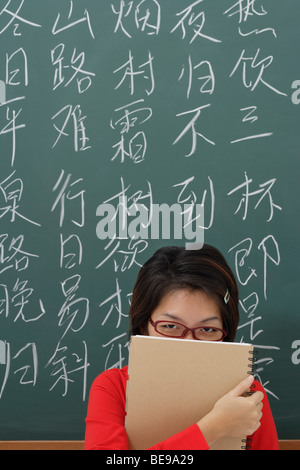 Studente di nascondersi dietro il blocco note nella parte anteriore dei caratteri cinesi scritti sulla scheda di Chalk Foto Stock