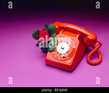 Telefono vintage 1970s rosso con rosa rossa Foto Stock