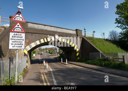 Indicazioni stradali per il traffico di guida unico file al di sotto di una altezza limitata ponte ferroviario in Inghilterra Foto Stock