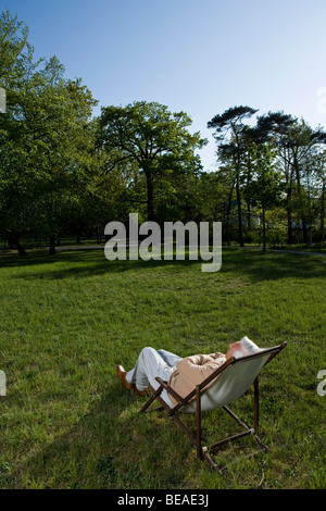 Un anziano uomo reclinata in una sedia a sdraio su un prato Foto Stock