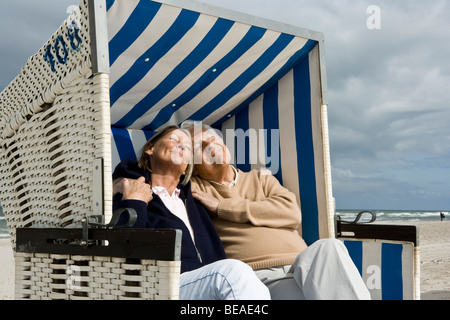 Una coppia senior seduti insieme in una spiaggia con cappuccio sedia Foto Stock