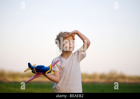 Un ritratto di una giovane ragazza con un aeroplano giocattolo e schermare gli occhi, all'aperto Foto Stock