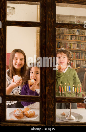 Bambini dietro una finestra di pioggia nella parte anteriore di un Hanukkia mangiare Jelly tradizionale ciambella in Hanukka Foto Stock