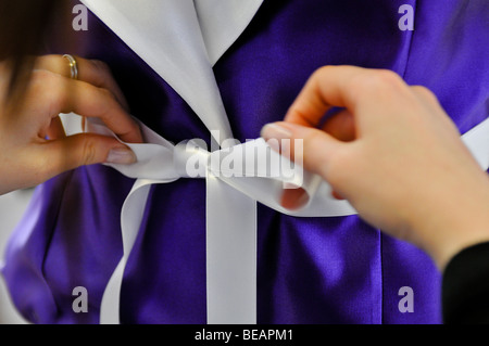 Giovane donna con le mani in mano la legatura di un nastro bianco su una camicetta viola. Foto Stock