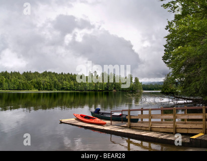 La zona di pesca in un lago delle Montagne Adirondack, con due canoe su un dock in legno Foto Stock