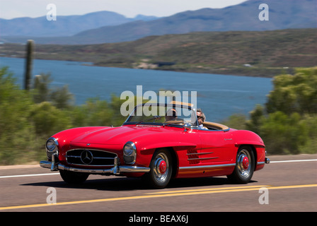 Un 1958 Mercedes Benz 300 SL Roadster guidando lungo una panoramica strada statale nei pressi di un lago. Foto Stock