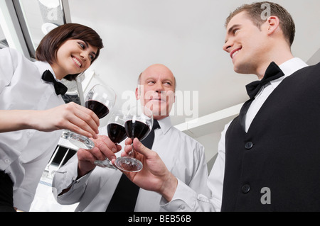 Due camerieri e una cameriera la tostatura con bicchieri di vino Foto Stock