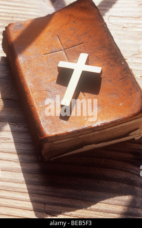 Close up della piccola pianura crocifisso metallica giacente su ben thumbed marrone pelle la Bibbia o il libro di preghiera sul davanzale di legno Foto Stock