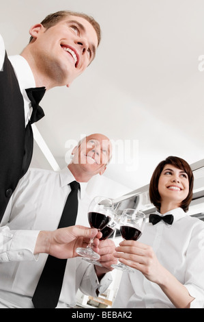 Due camerieri e una cameriera la tostatura con bicchieri di vino Foto Stock