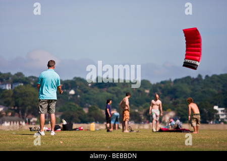 Un uomo rilassante battenti un rosso sparless kite in piscina Quay park su una soleggiata giornata d'estate. Altre persone rilassarsi in background. Foto Stock