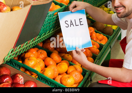 Venditore mostrando un cartello di vendita su frutta' casse Foto Stock