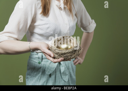 Metà vista in sezione di una donna tenendo un uovo dorato nel nido Foto Stock