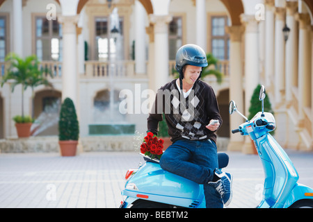 Uomo seduto su un ciclomotore e messaggistica di testo su un telefono cellulare, Biltmore Hotel Coral Gables, Florida, Stati Uniti d'America Foto Stock