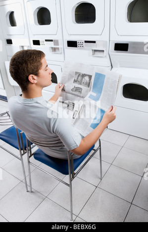 L'uomo leggendo un giornale in una lavanderia a gettoni Foto Stock
