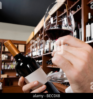 Mano d'uomo tenendo un bicchiere di vino e una bottiglia di vino Foto Stock