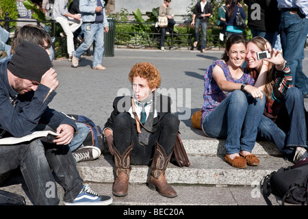 Giovane folla di persone godendo la lettura rilassante e scattare fotografie in una soleggiata Union Square Park di New York City Foto Stock
