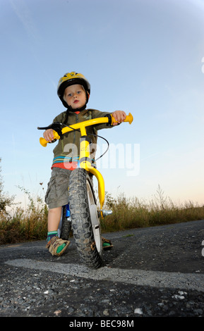 Bambino ragazzo in bicicletta attraverso una foresta corsa in bicicletta con il casco protettivo Foto Stock