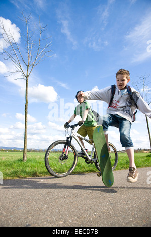 Un ragazzo con uno skateboard e un ragazzo su una mountain bike in campagna Foto Stock
