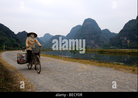 Donna vietnamita in bicicletta nel cestino di raccolta di fronte montagne carsiche, Parco Nazionale TamCoc, Ninh Binh, Vietnam del Nord, Sud Foto Stock