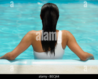 Vista posteriore di una donna appoggiata contro il lato di una piscina Foto Stock