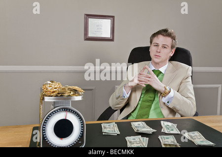 Imprenditore seduto di fronte a moneta note con gioielli in oro su una scala di peso Foto Stock