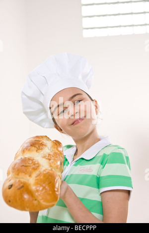 Ragazza che indossa un chef hat tenendo un intrecciato bun lievito in mano Foto Stock