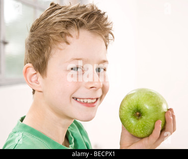 Ragazzo che sorride tenendo una mela verde nella parte anteriore del suo volto Foto Stock