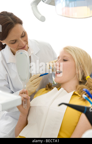 Controllo del dentista una ragazza i denti, ragazza guardando con uno specchio a mano Foto Stock