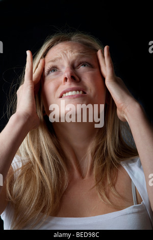 Giovane donna bionda che tiene i suoi templi come ella è mostra lo stress o dolore Foto Stock