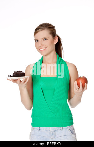 Carino donna caucasica cercando di prendere una decisione tra il mangiar sano o non Foto Stock