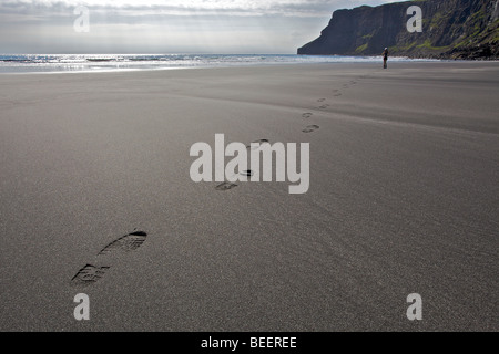 Una femmina di escursionista passeggiate lungo una spiaggia lasciando tracce nella sabbia Foto Stock