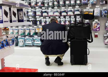 Un passeggero si china a ispezionare gli adattatori da viaggio e tappi di Dixons Digital in aeroporto di Heathrow il terminal 5 Foto Stock