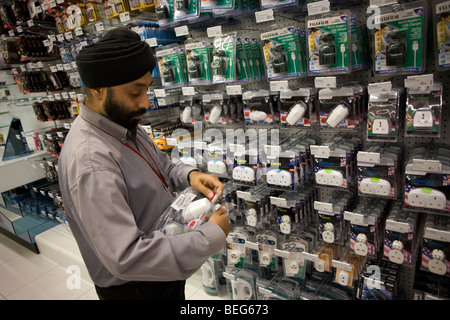 Un assistente di vendita con Dixons Digital rifornisce ripiani con adattatori da viaggio e tappi a Heathrow airport del terminale 5 Foto Stock